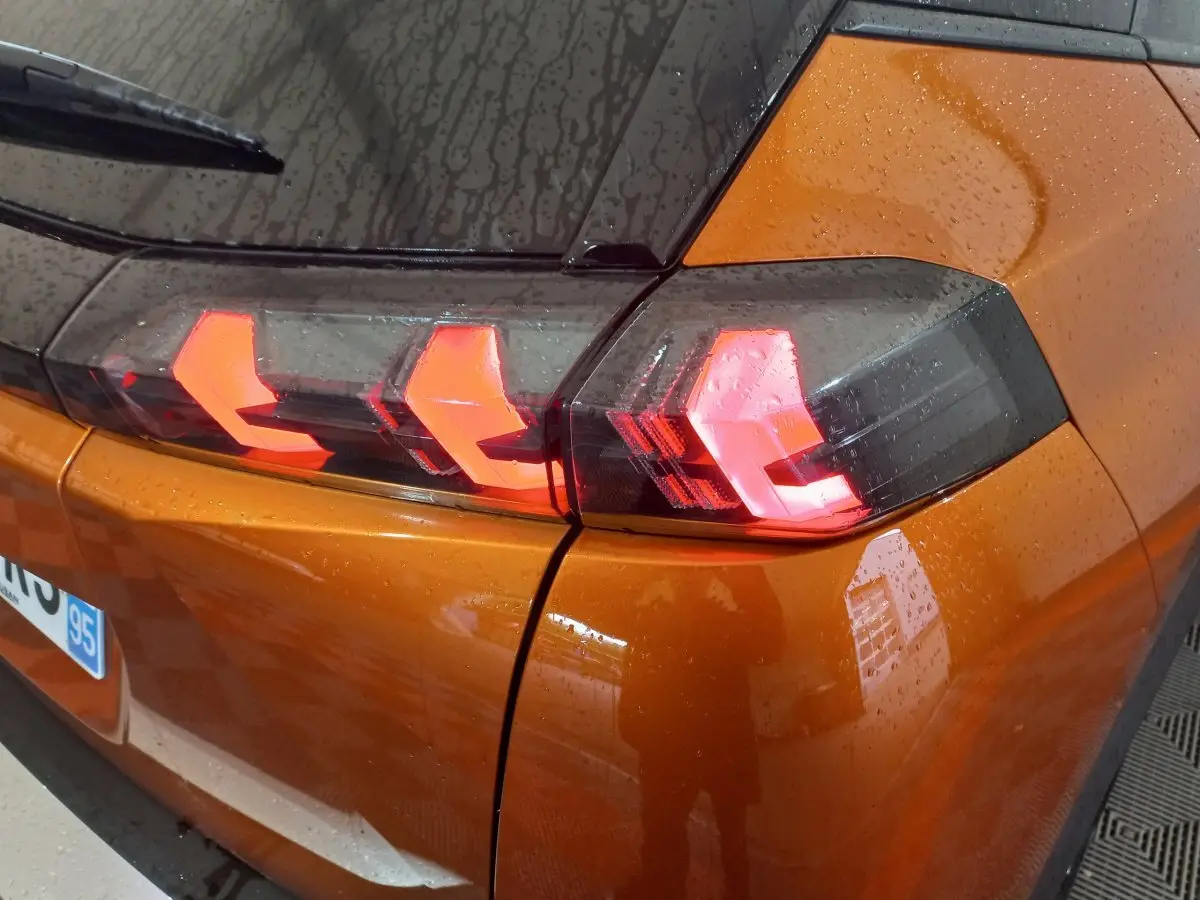 Gros plan sur le feu arrière gauche allumé d’un Peugeot 2008 orange 2021 sous la pluie.
