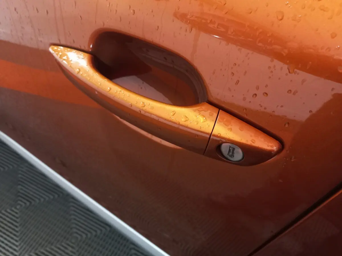 Poignée de porte avant droite orange métallisé de Peugeot 2008 BlueHDi 110 S&S Allure Business 2021 avec gouttes d'eau visibles.