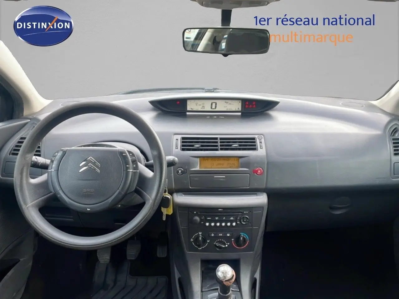 Vue intérieure avant centrée sur le tableau de bord gris et volant de la Citroën C4 Coupé noir métal de 2009 avec boîte manuelle.