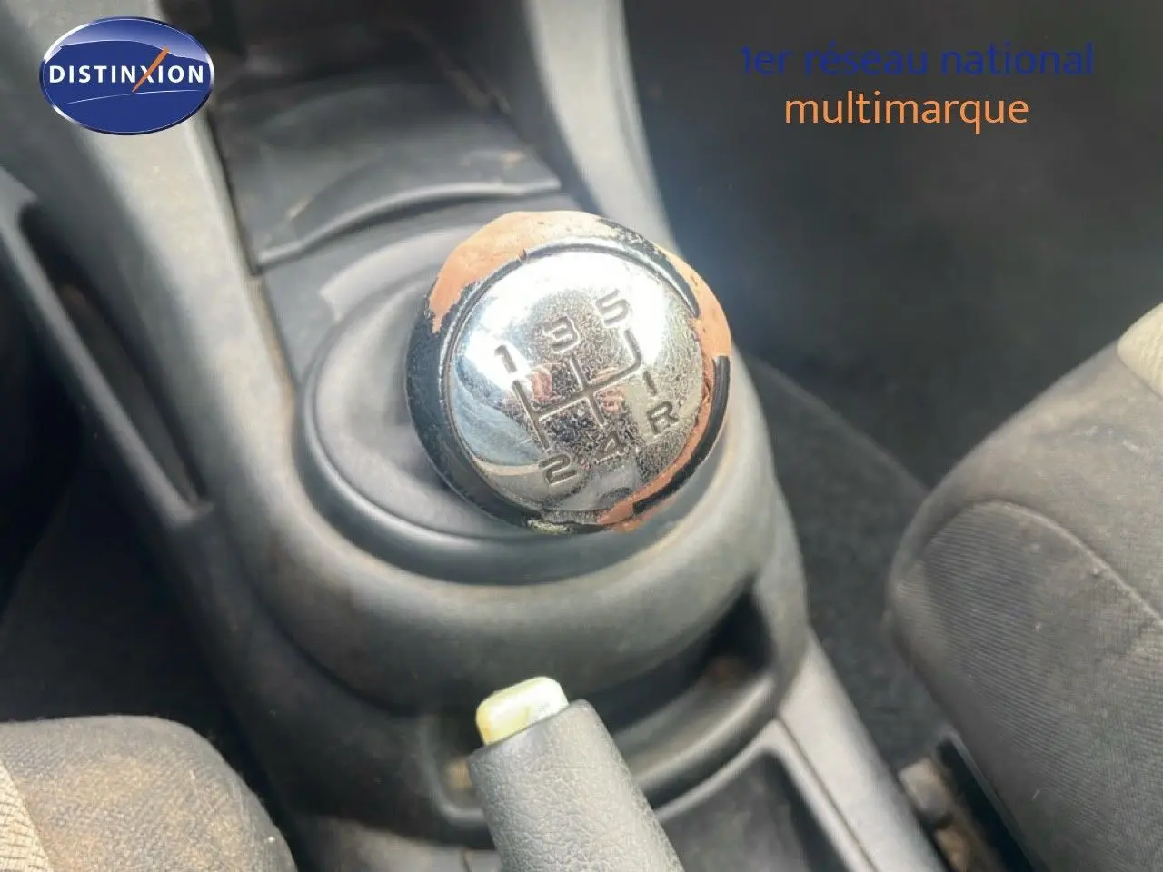 Gros plan sur le levier de vitesse manuel usé de la Citroën C4 Coupé noir métal de 2009, intérieur tissu gris visible.