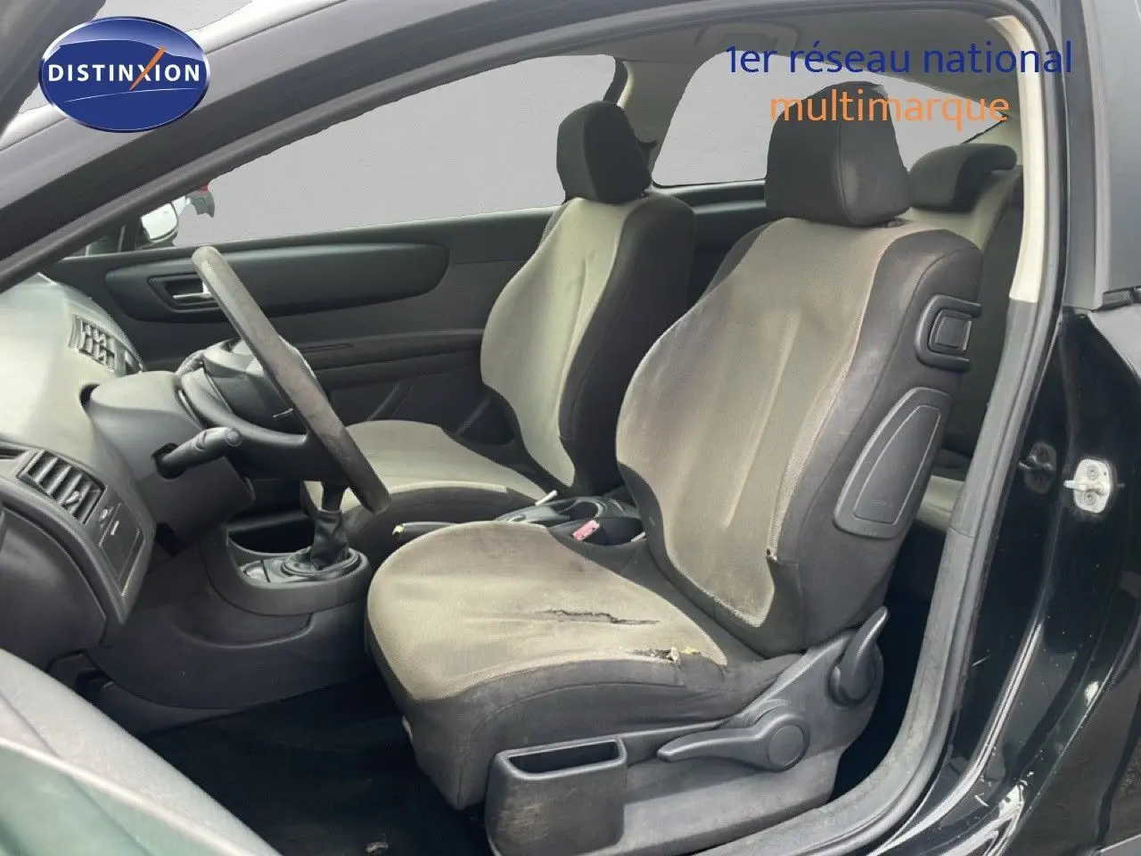 Vue intérieure côté gauche montrant les sièges avant gris tissu et volant d'une Citroën C4 Coupé noir métal 2009.
