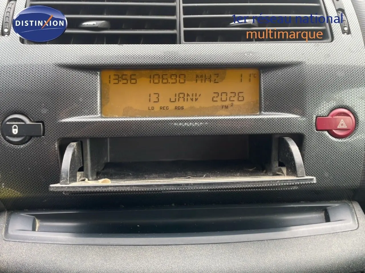 Vue rapprochée du tableau de bord de la Citroën C4 Coupé 2009, affichage radio orange et bouton rouge d'alerte visible.