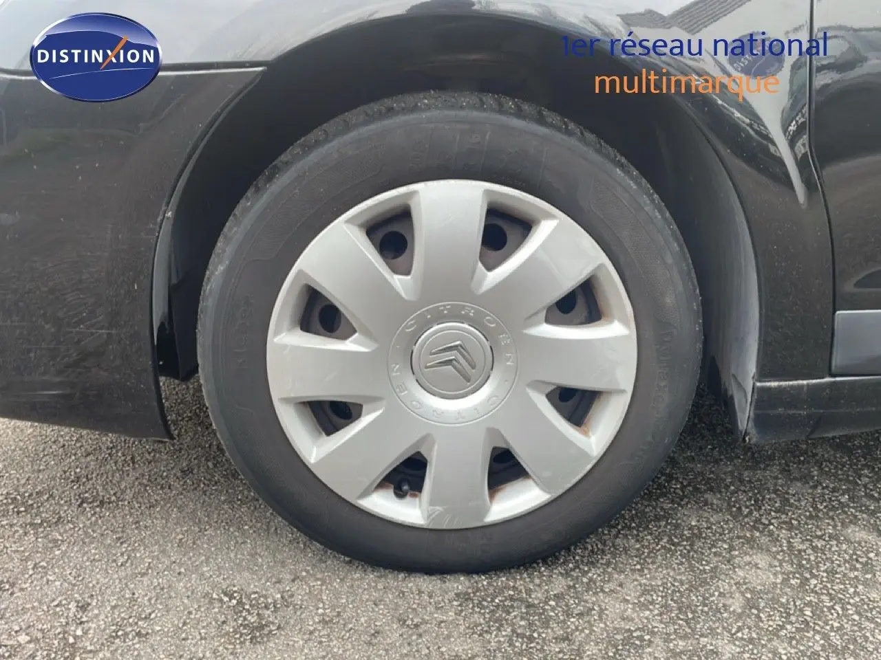 Gros plan sur la roue avant gauche d'une Citroën C4 Coupé 2009 noir métal avec enjoliveur gris.