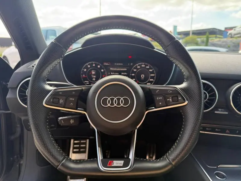 Vue centrée sur le volant sport cuir noir avec logo Audi et badge S line, tableau de bord numérique en arrière-plan.
