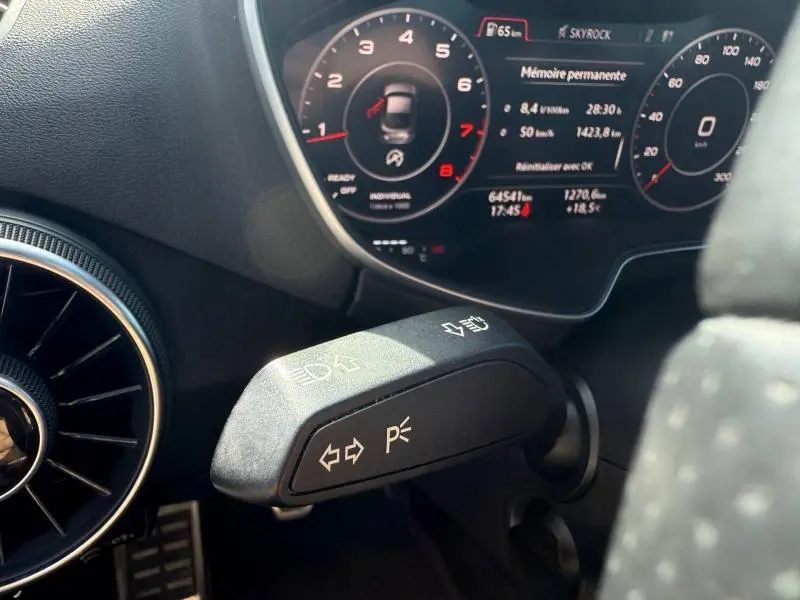 Gros plan sur la manette de clignotants noire et le tableau de bord numérique d'une Audi TT Coupé 2016, intérieur noir.