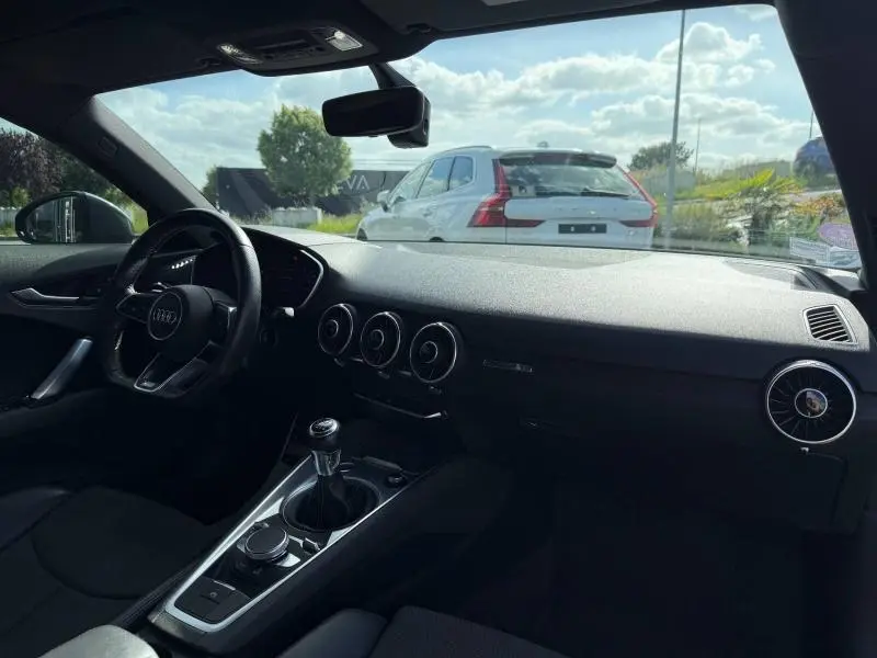 Vue intérieure côté conducteur de l'Audi TT Coupé 2016 noire, mettant en valeur le tableau de bord et la boîte manuelle.