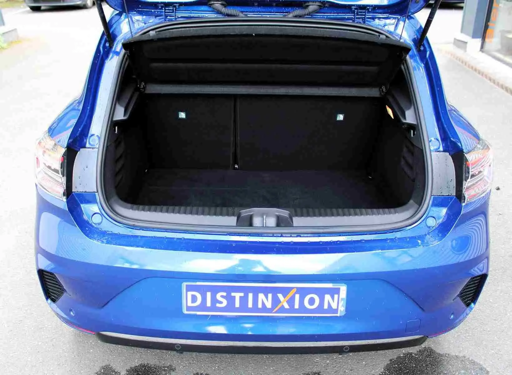 Coffre ouvert vu de l'arrière d'une Renault Clio 2025 bleu iron metal, montrant l'espace de chargement vide.