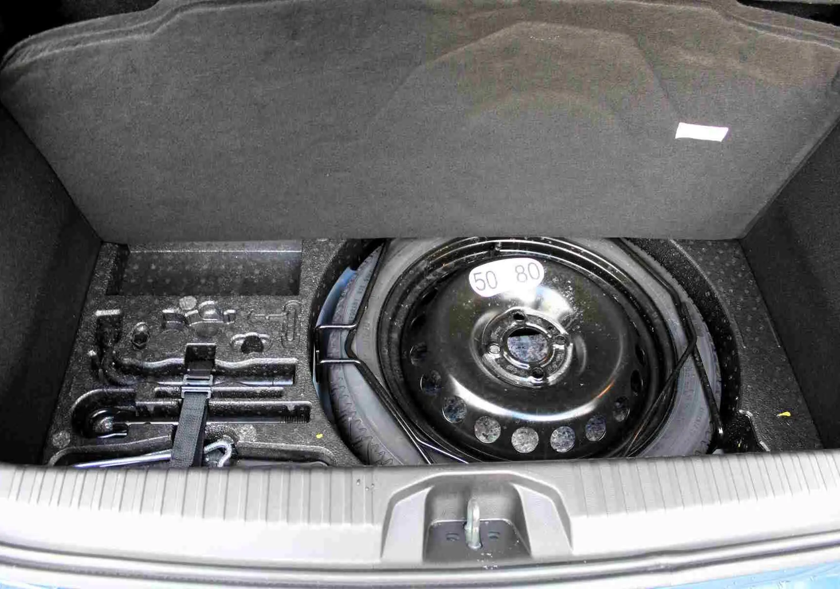 Coffre ouvert d’une Renault Clio bleu Iron Metal 2025, montrant la roue de secours et les outils de bord.