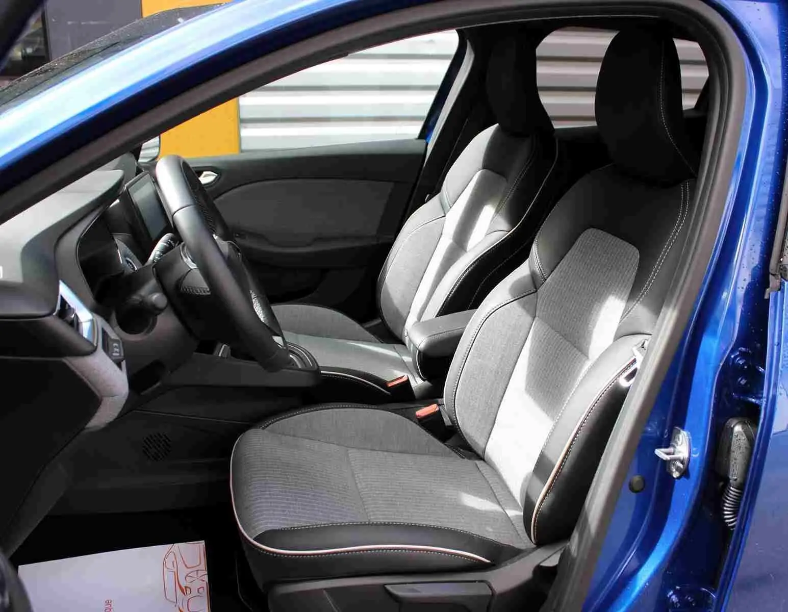 Vue intérieure côté conducteur de la Renault Clio 2025 bleu Iron Metal, sièges tissu gris noir avec surpiqûres contrastées.