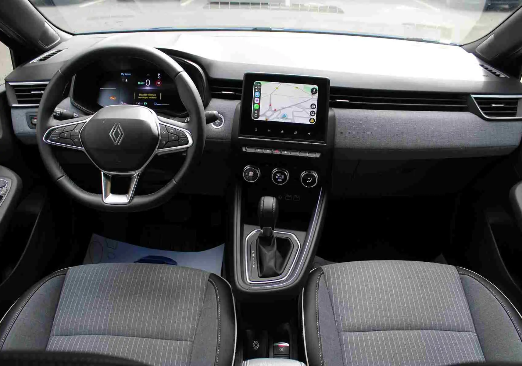 Vue intérieure avant de la Renault Clio hybride 2025, tableau de bord gris noir avec écran tactile central et volant multifonction.