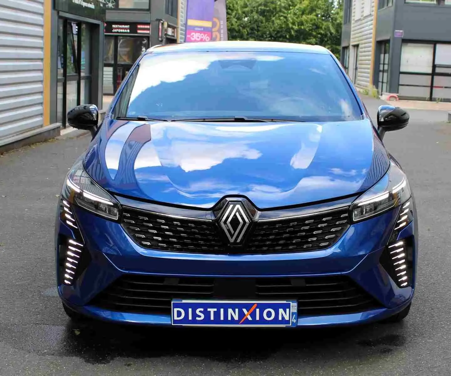 Vue frontale d'une Renault Clio 2025 bleu iron metal avec calandre noire et feux LED verticaux allumés.