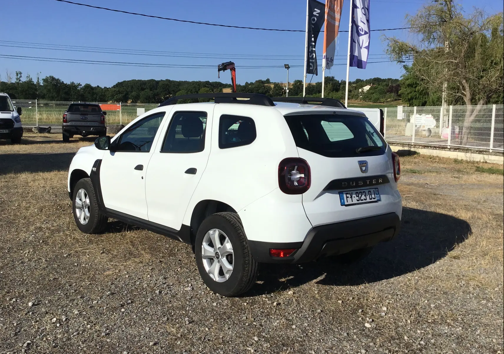 Vue 3/4 arrière droite d'un Dacia Duster blanc 4x2 ECO-G 100 Essentiel avec barres de toit et feux arrière LED.