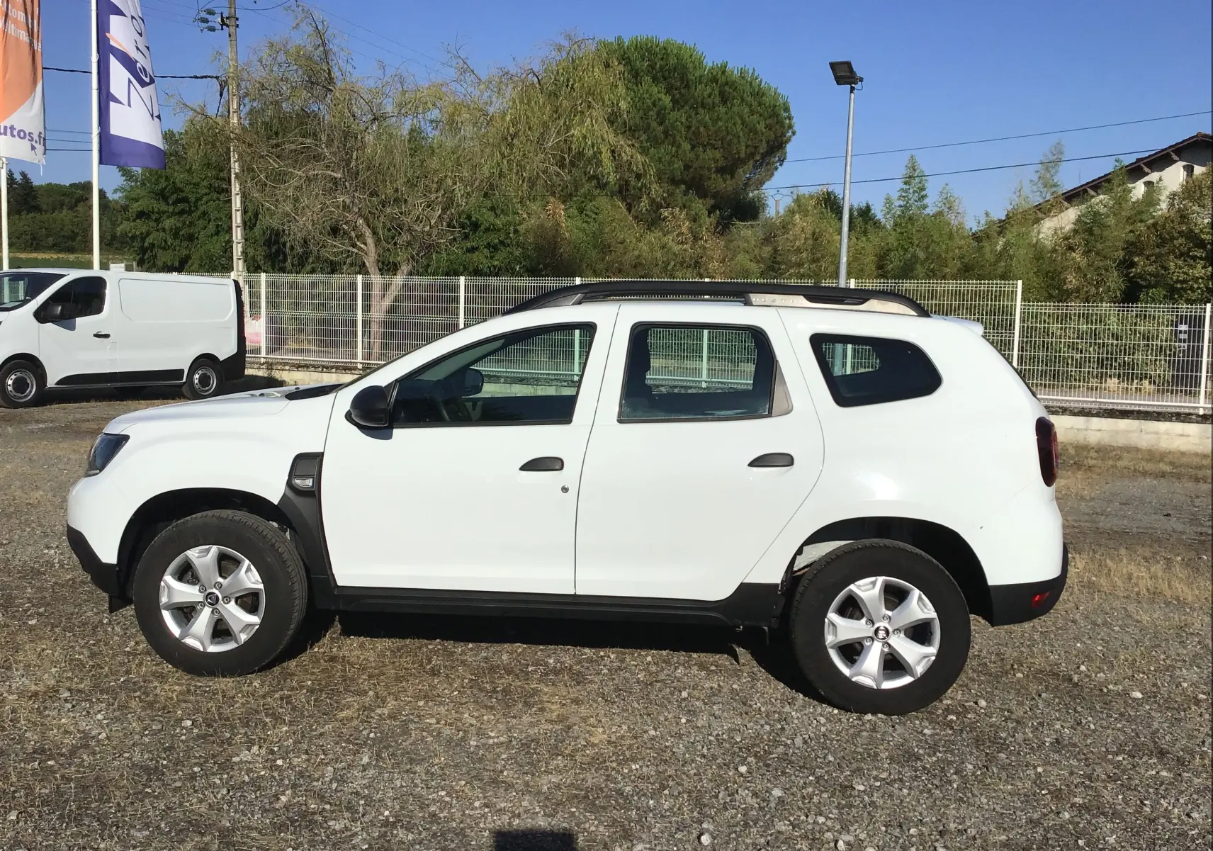 Profil côté gauche d'un Dacia Duster blanc 4x2 Eco-G 100 Essentiel de 2021 avec barres de toit et jantes alliage.