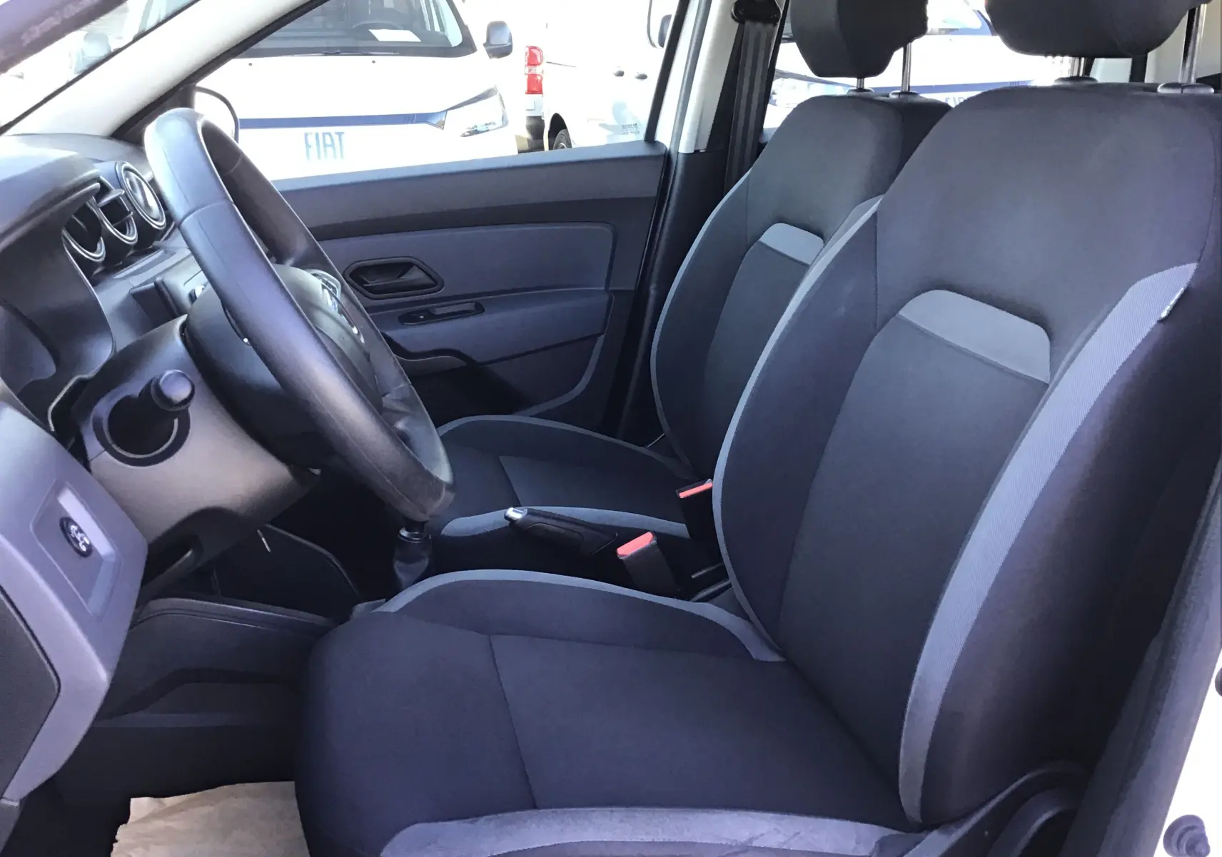 Vue intérieure côté conducteur du Dacia Duster 2021, sièges noirs avec détails gris et volant visible.