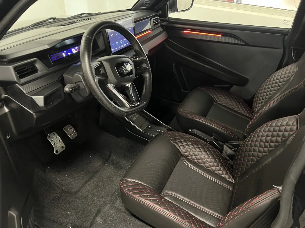 Vue intérieure côté conducteur du Ligier JS50 2026, sièges noirs avec surpiqûres rouges et tableau de bord digital lumineux.