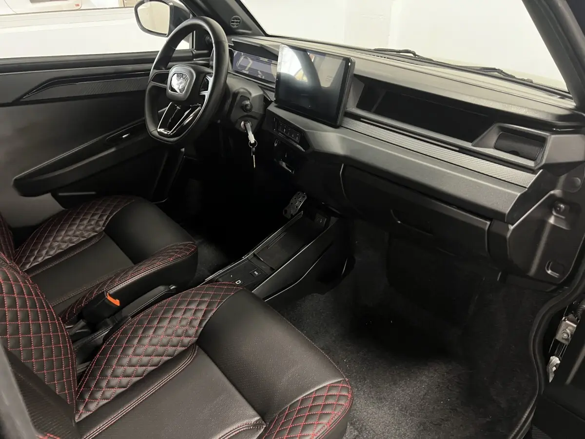 Intérieur avant droit de la LIGIER JS50 0.5 REVO D+ ULTIMATE 2026, sièges noirs avec surpiqûres rouges et écran tactile central.