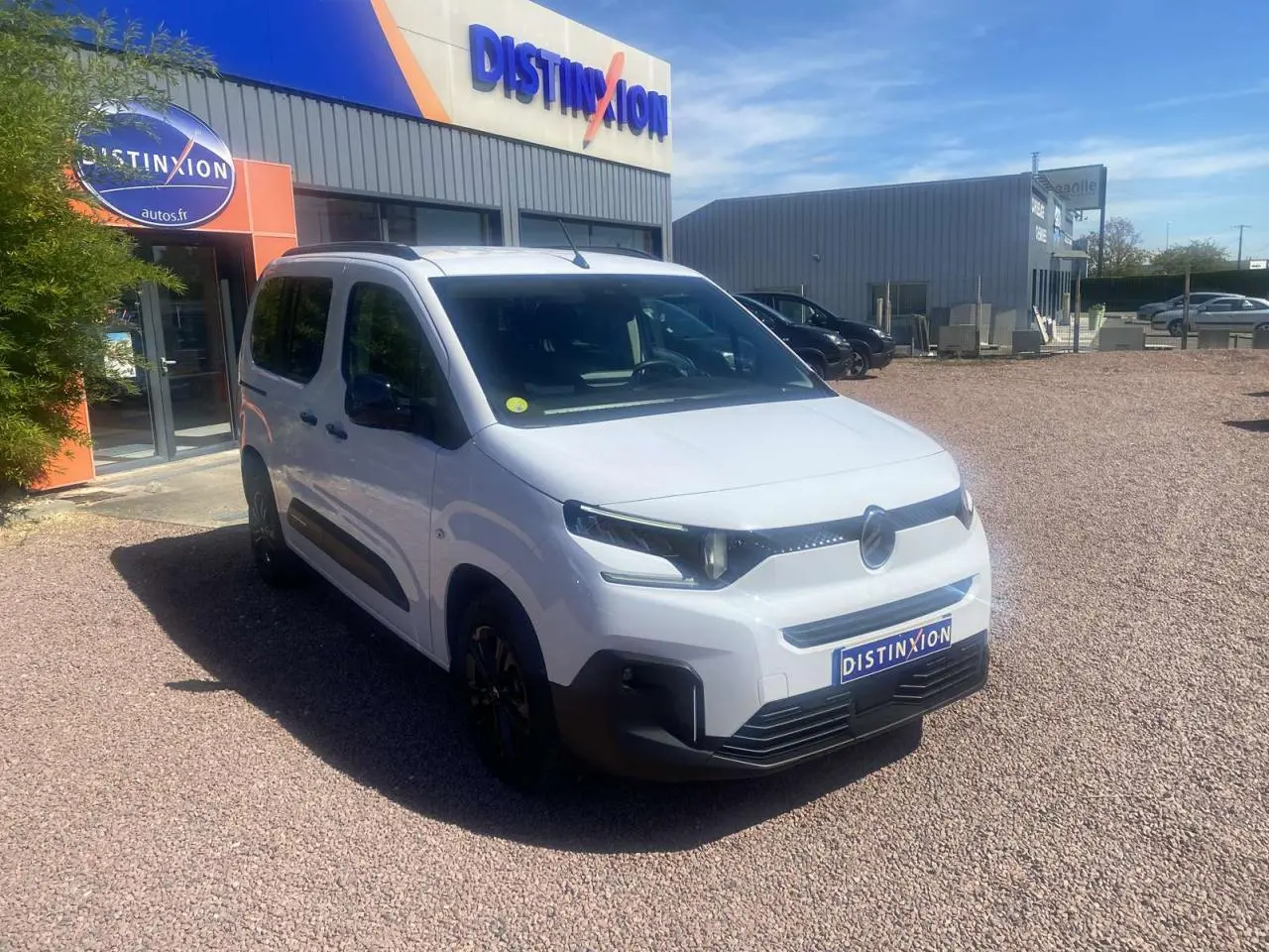 Vue 3/4 avant d'un Citroën Berlingo blanc 2025 avec portes coulissantes, stationné devant un bâtiment Distinxion.