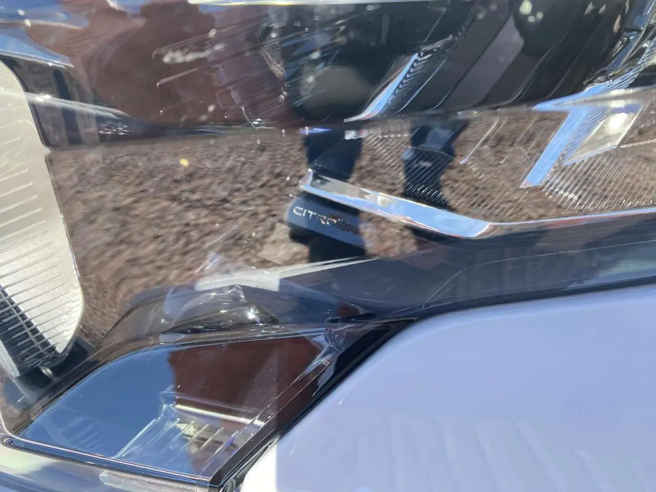 Gros plan sur le phare avant droit du Citroën Berlingo blanc 2025 avec détails chromés et marquage CITROËN visible.