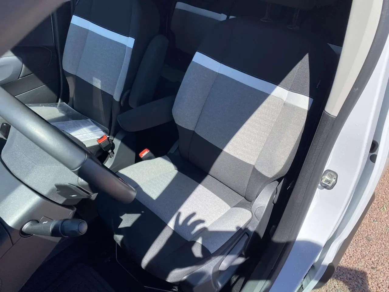 Vue intérieure côté conducteur du Citroën Berlingo blanc 2025, montrant les sièges avant en tissu gris bicolore.