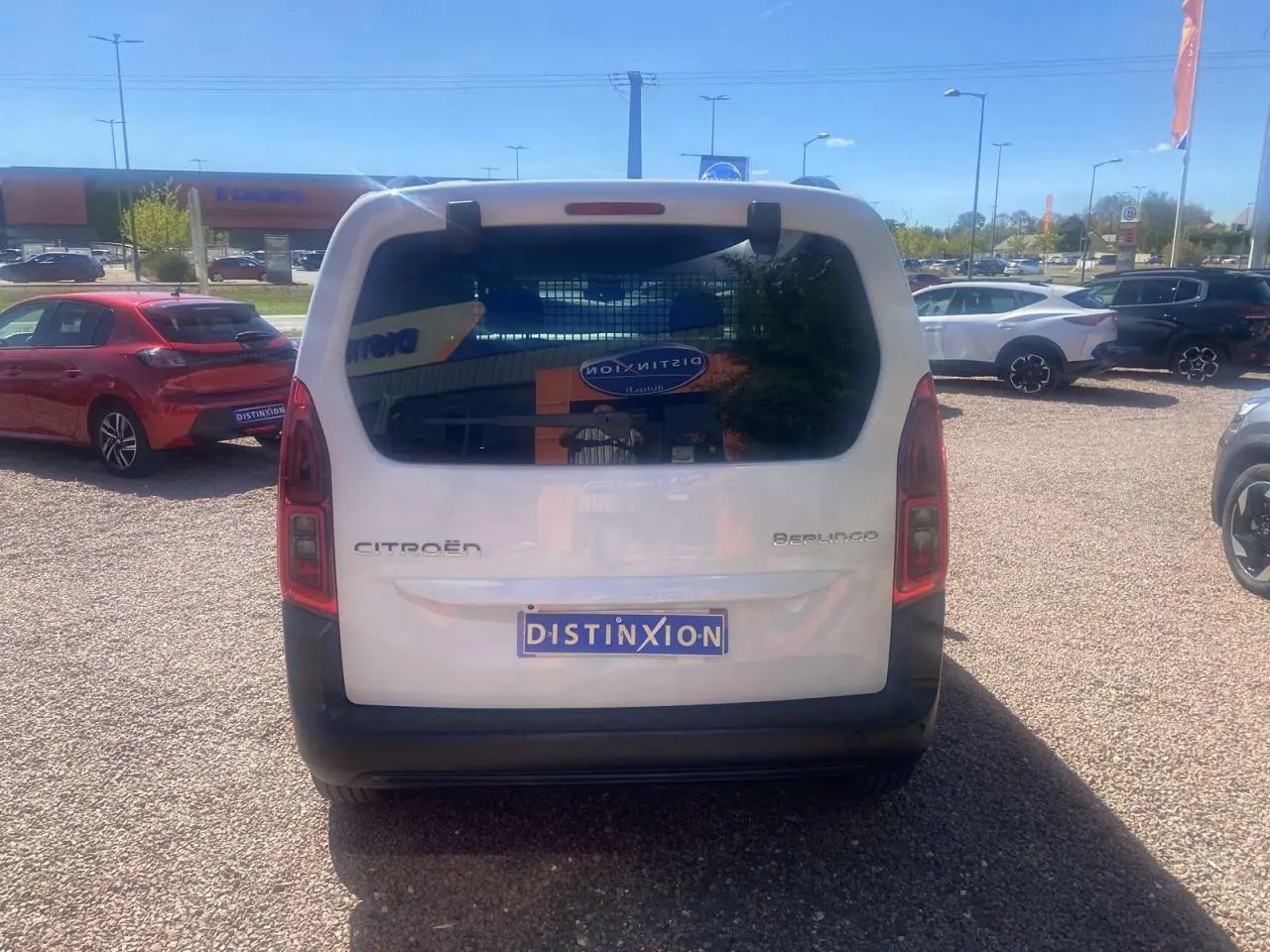 Vue arrière d'un Citroën Berlingo blanc 2025 avec hayon vitré et plaque Distinxion sur un parking extérieur.