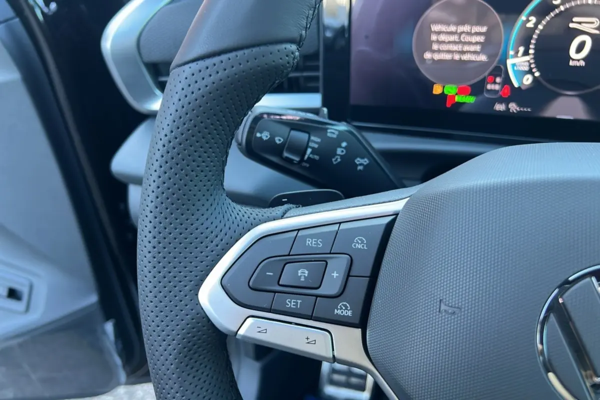 Gros plan sur le volant cuir noir perforé du Volkswagen T-Roc 2026 avec commandes multifonctions et affichage digital en arrière-plan.