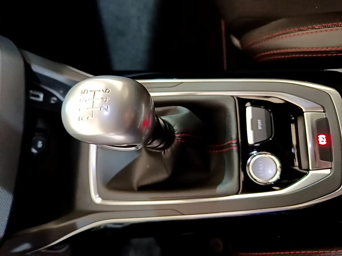 Gros plan sur levier de vitesses manuel argenté et console centrale noire avec surpiqûres rouges dans Peugeot 308 gris foncé.