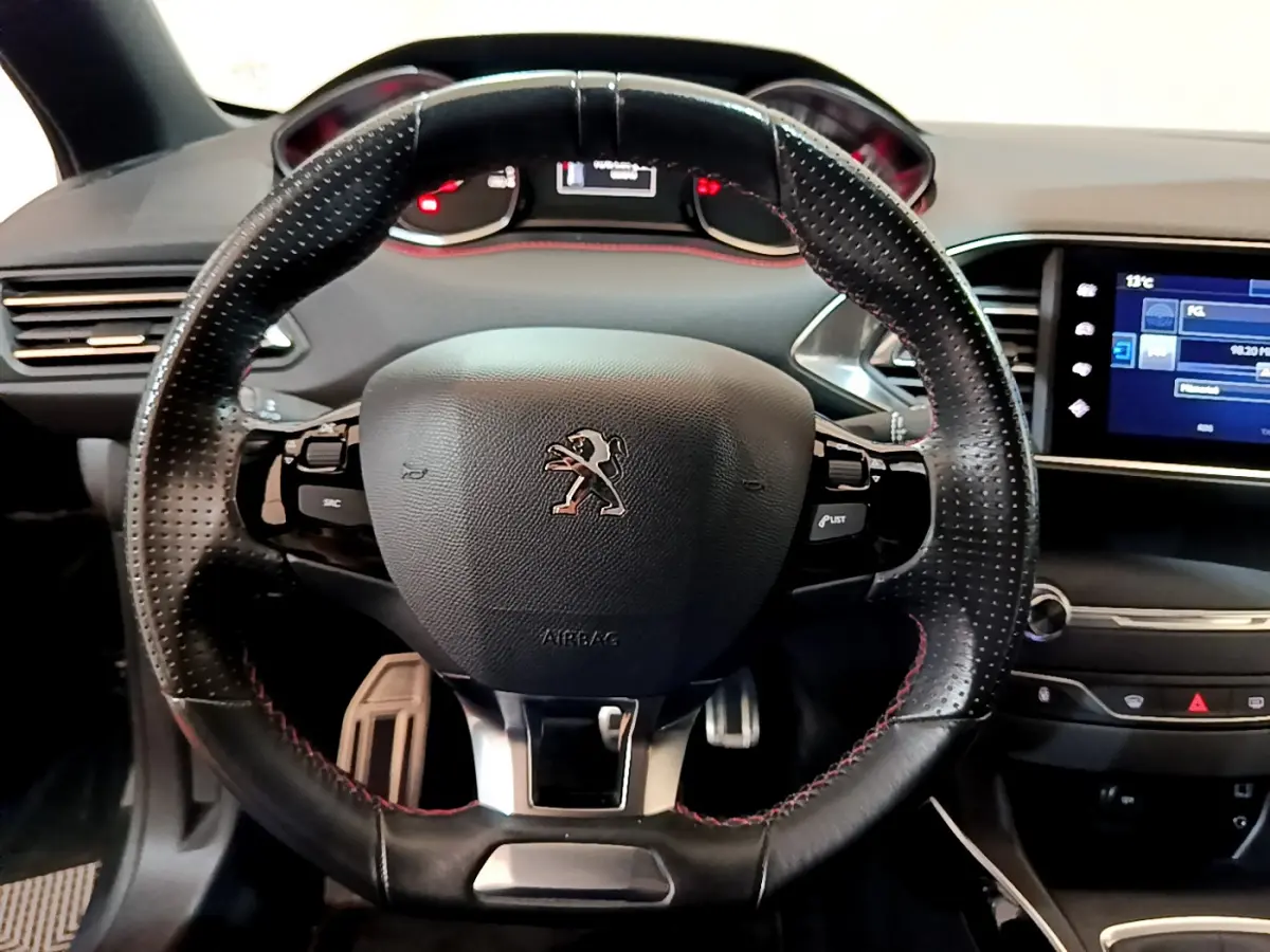 Vue centrée sur le volant cuir perforé avec surpiqûres rouges de la Peugeot 308 GT Line 2016, tableau de bord et écran tactile visibles.