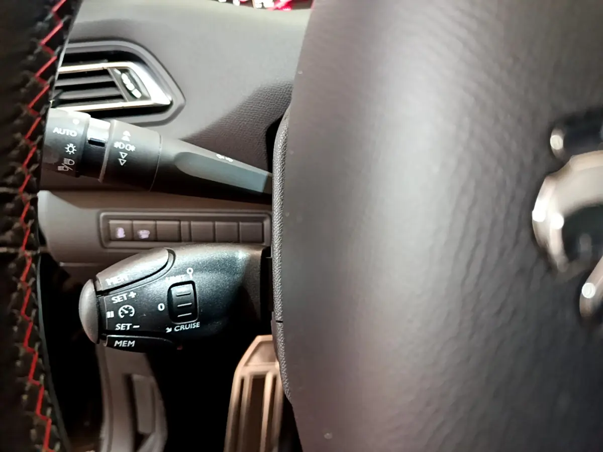 Gros plan sur la commande de régulateur de vitesse à gauche du volant cuir noir d'une Peugeot 308 gris foncé.