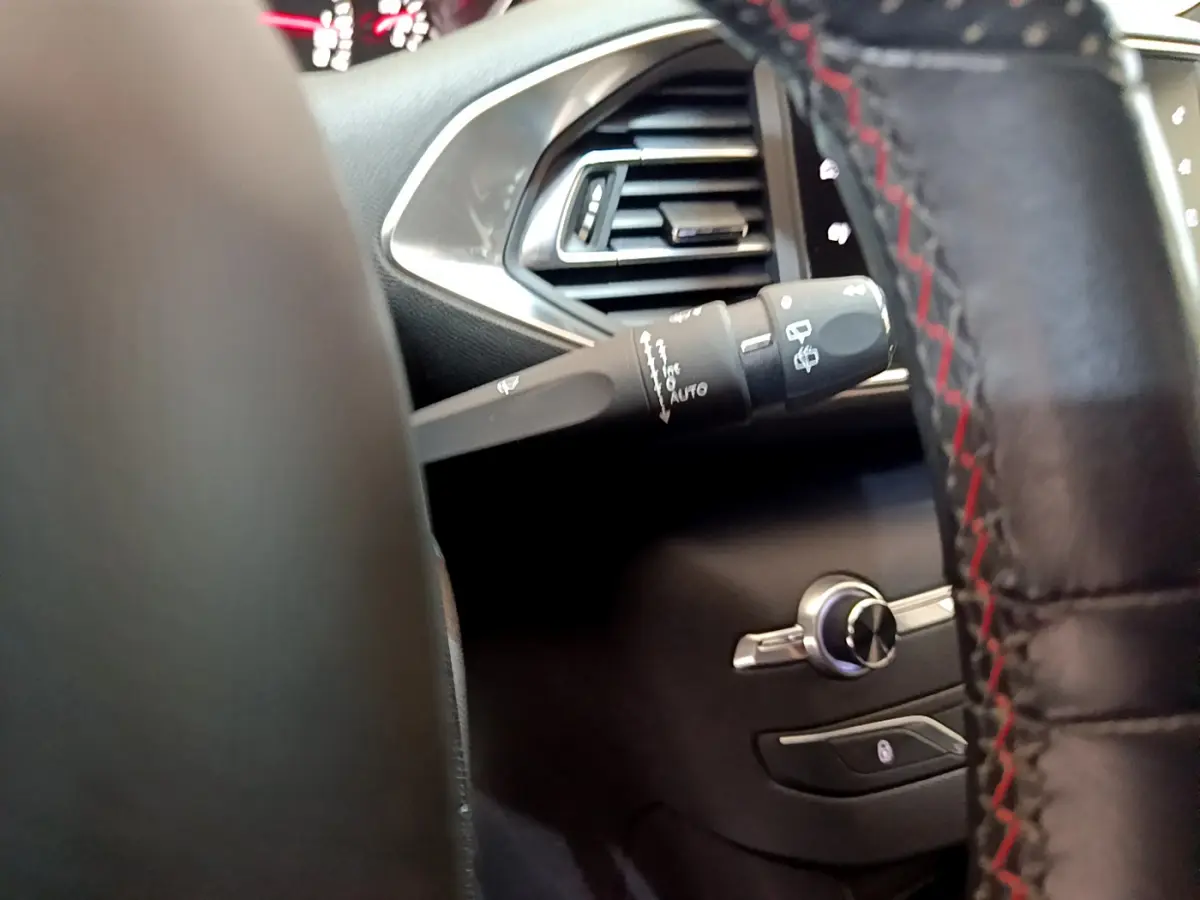 Gros plan sur la commande d’essuie-glace et la sortie d’air côté gauche du tableau de bord noir du Peugeot 308 gris foncé.