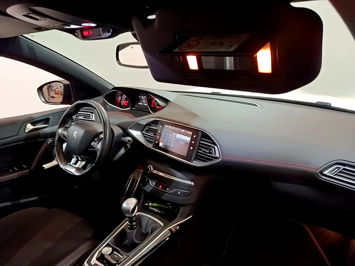 Vue intérieure côté conducteur du tableau de bord et volant cuir d'une Peugeot 308 gris foncé avec écran tactile central allumé.