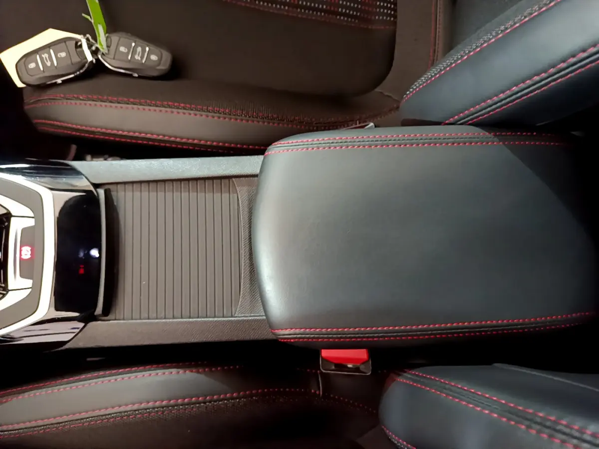 Vue plongeante sur la console centrale en cuir noir avec surpiqûres rouges et clés de Peugeot 308 gris foncé posées sur le siège.