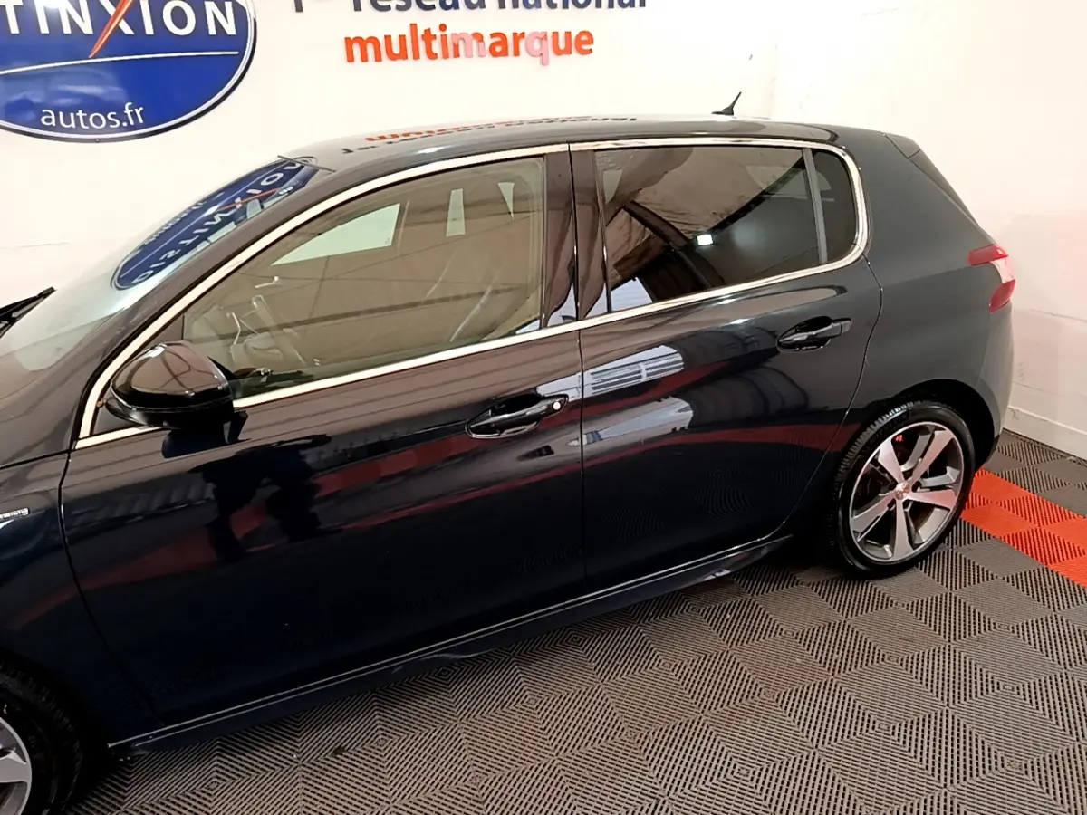 Profil côté gauche d'une Peugeot 308 gris foncé, avec jantes alliage et vitres teintées en intérieur showroom.
