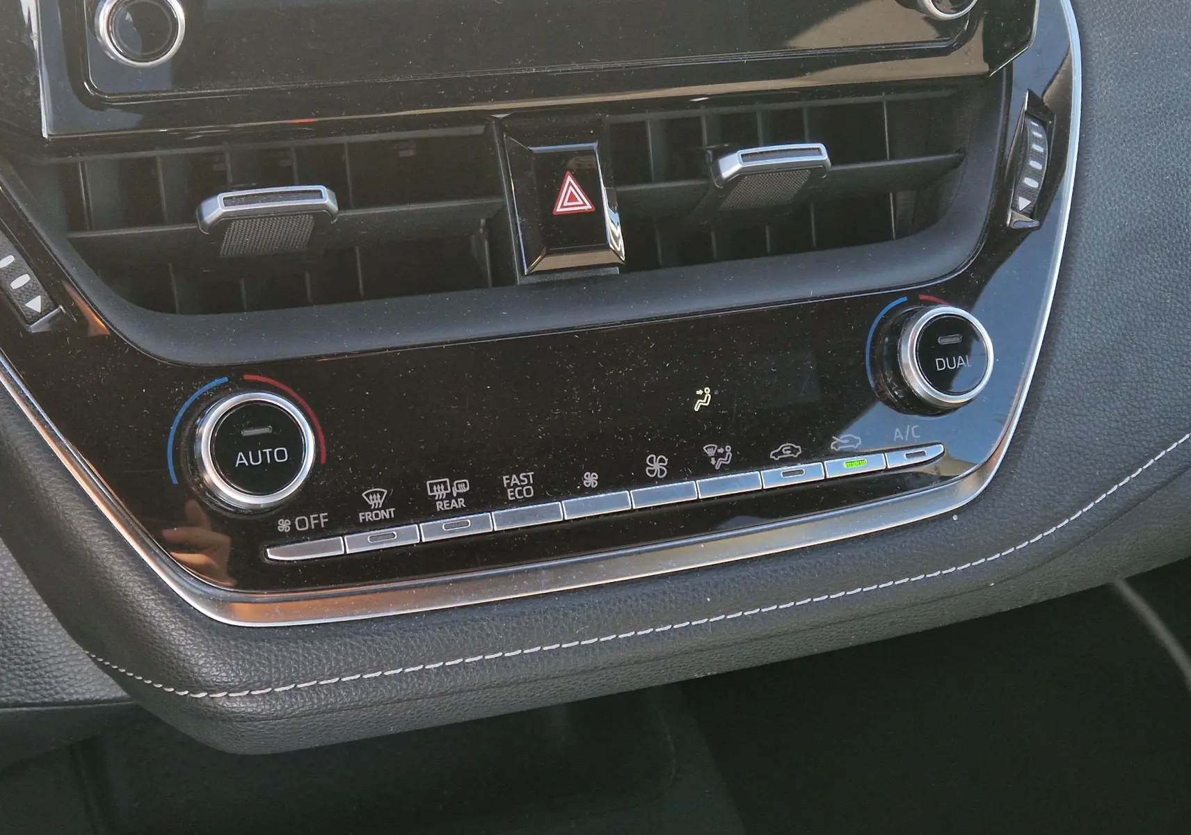 Vue rapprochée de la console centrale noire de la Toyota Corolla Hybride 122h Design, avec commandes climatisation et boutons lumineux.