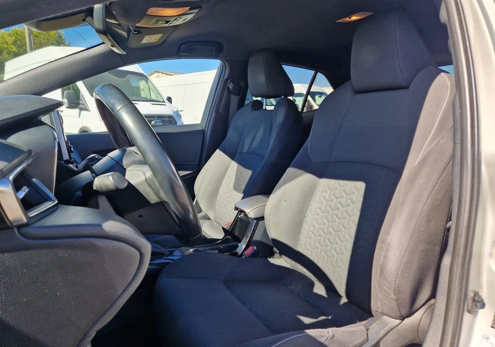 Vue intérieure côté conducteur de la Toyota Corolla hybride 2019, sièges tissu gris et volant noir.