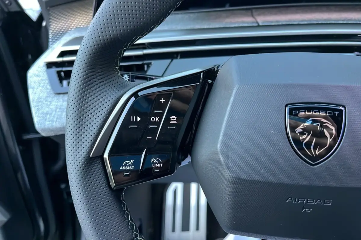 Gros plan sur le volant cuir perforé du Peugeot 5008 Hybrid 2025, avec commandes multifonctions et logo lion noir.