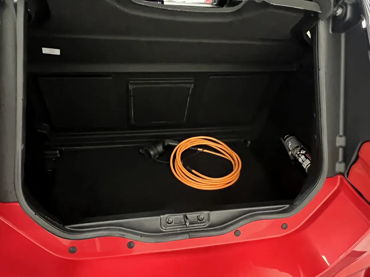 Vue plongeante sur le coffre ouvert rouge d'une LIGIER JS50 BEV 8KWH ELITE avec câble de charge orange à l'intérieur.