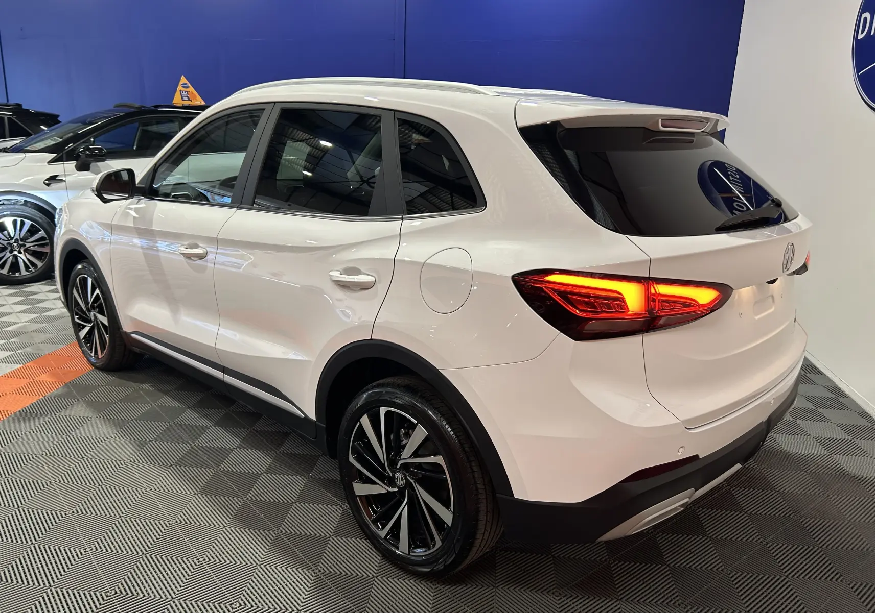 Vue 3/4 arrière droite du MG ZS Hybrid+ 197 Luxury blanc Dover avec toit panoramique ouvrant en intérieur showroom.