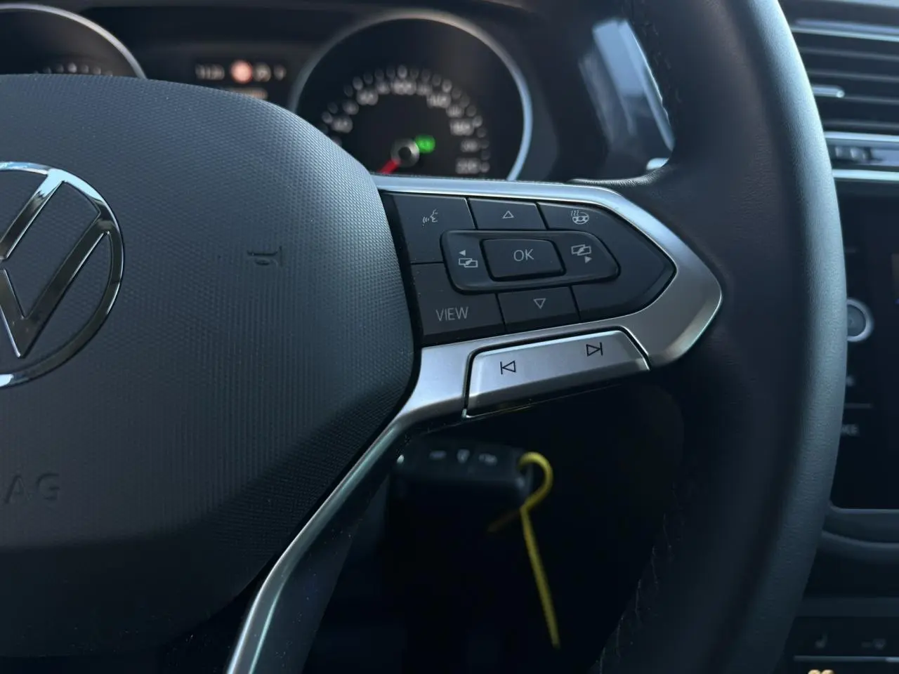 Gros plan sur le volant multifonctions cuir du Volkswagen Tiguan 2024, boutons de commande et logo VW visibles.