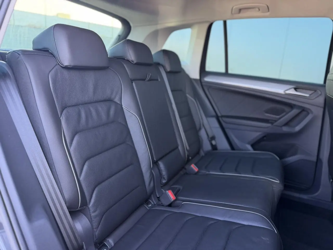 Vue latérale droite de la banquette arrière en cuir noir du Volkswagen Tiguan 2024 avec surpiqûres claires et vitres surteintées.