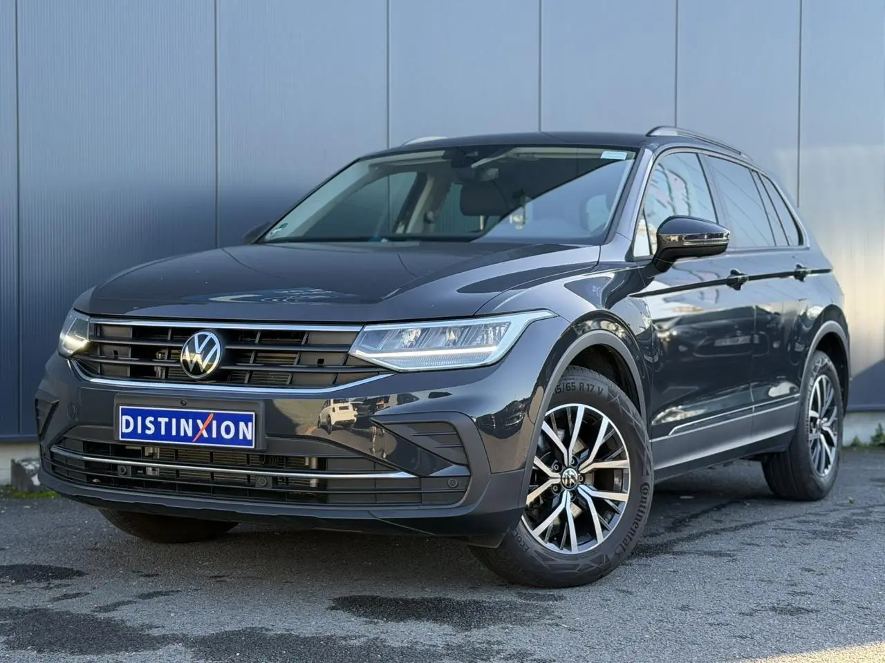 Volkswagen Tiguan 1.5 TSI gris Urano en 3/4 avant droit, avec jantes alliage et calandre distinctive.