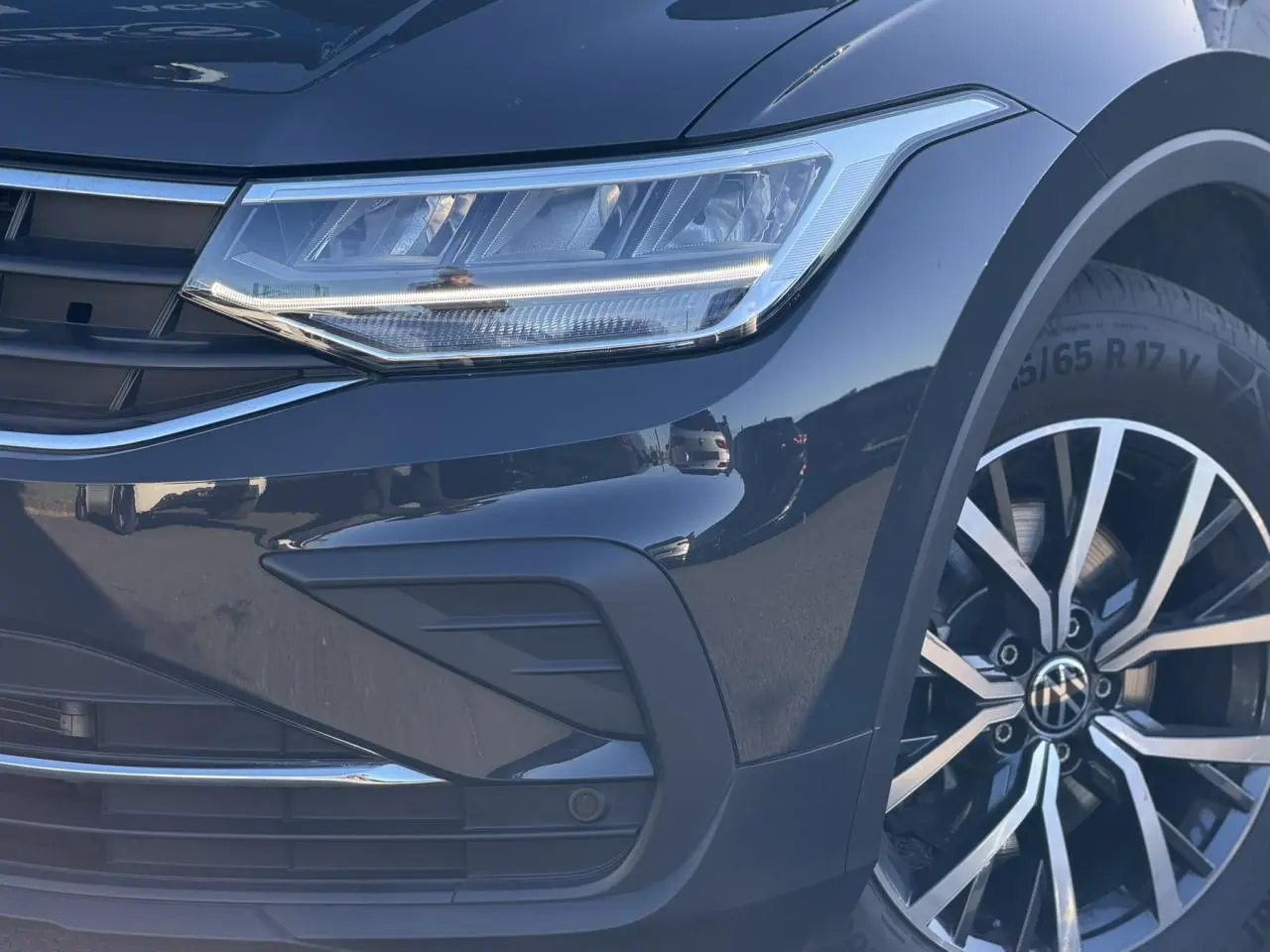 Gros plan sur l'avant droit du Volkswagen Tiguan gris Urano, mettant en valeur le phare LED et la jante alliage 17 pouces.