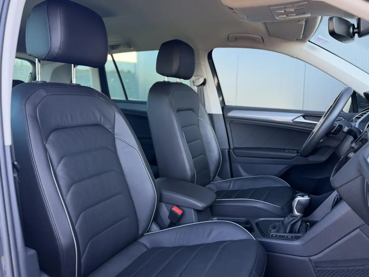 Vue intérieure côté gauche du Volkswagen Tiguan 2024, sièges cuir Vienna noirs avec surpiqûres grises et console centrale.