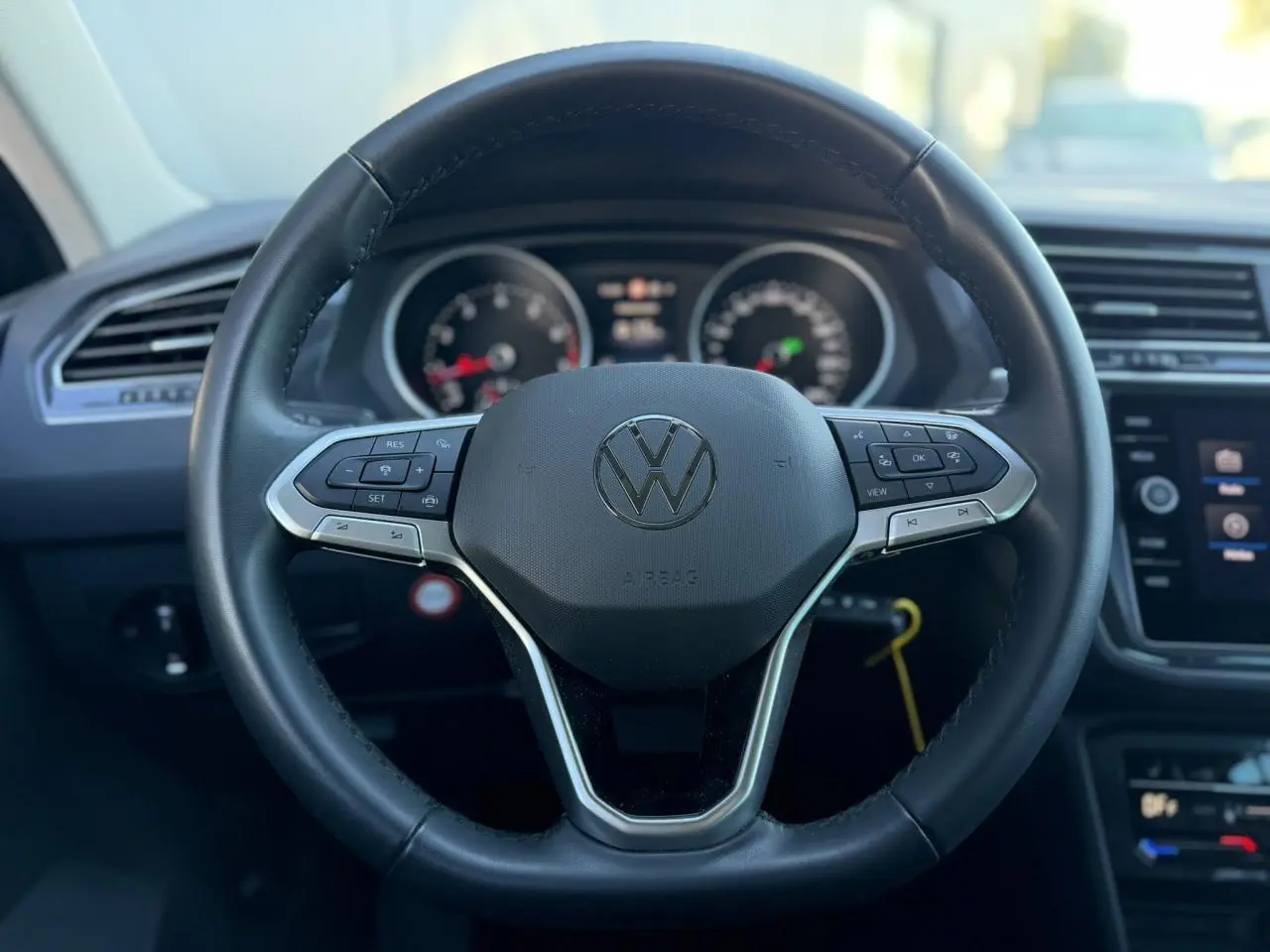 Gros plan sur le volant cuir multifonctions noir du Volkswagen Tiguan 2024 avec tableau de bord et écran tactile en arrière-plan.
