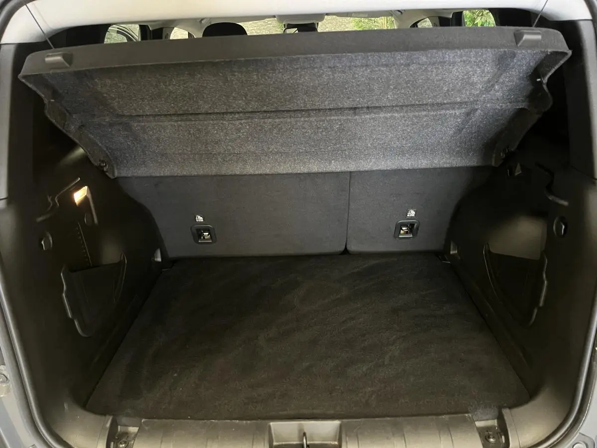 Coffre ouvert du Jeep Renegade gris 2024 montrant le plancher modulable et les rangements latéraux noirs.