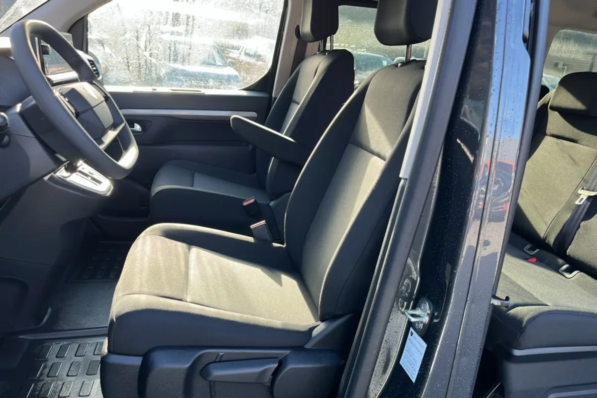 Vue intérieure côté conducteur du Peugeot Traveller gris titane 2025, sièges avant avec accoudoir central et volant multifonctions.