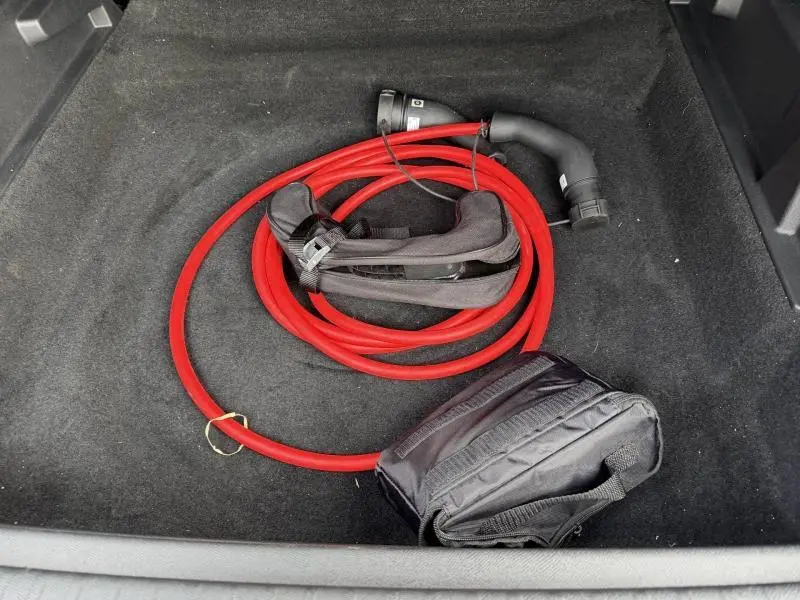 Coffre ouvert d’un Peugeot 3008 électrique 2024 montrant un câble de recharge rouge et une sacoche noire.