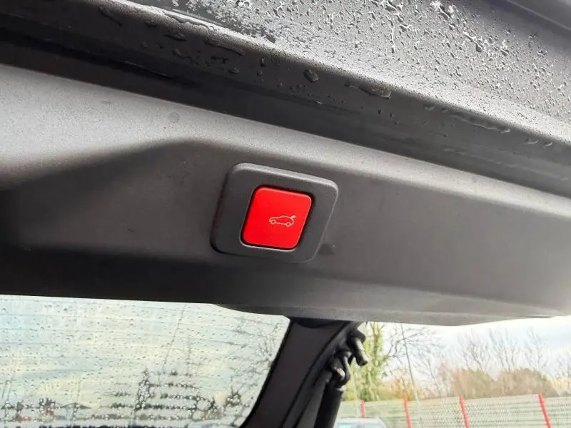 Bouton rouge d'ouverture électrique du coffre visible sur la partie intérieure du hayon d'un Peugeot 3008 bleu.