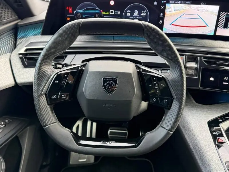 Vue intérieure centrée sur le volant cuir GT et les écrans numériques du tableau de bord du Peugeot 3008 bleu électrique 2024.