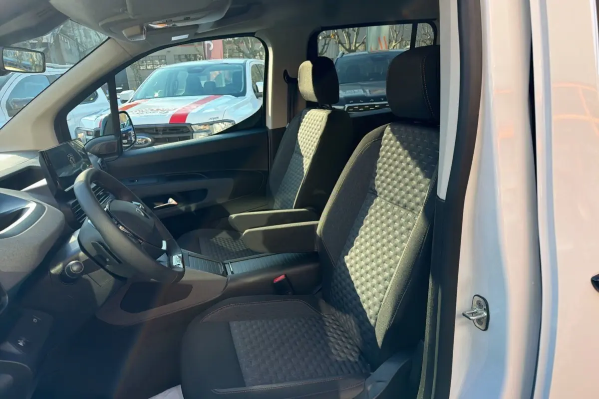 Vue intérieure côté conducteur du Peugeot Rifter blanc kaolin 2025, sièges tissu avec accoudoirs et volant cuir multifonctions.