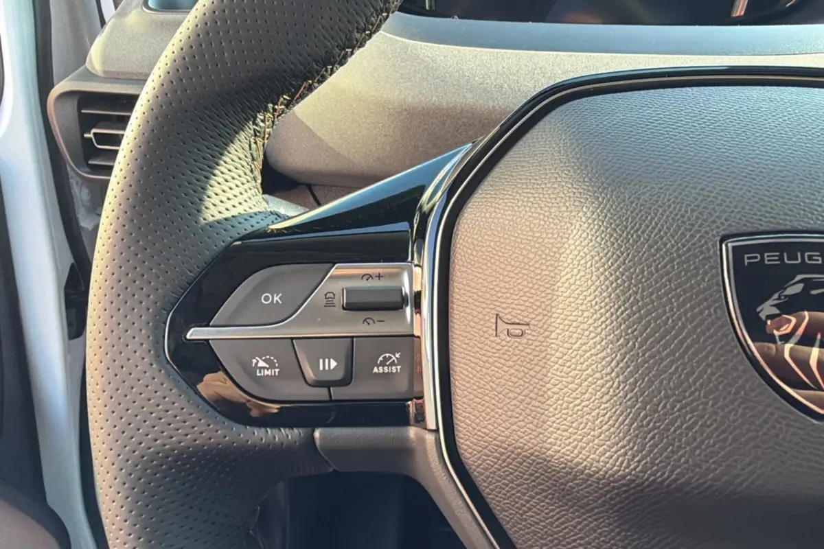 Gros plan sur le volant cuir perforé côté gauche du Peugeot Rifter Blanc Kaolin, avec commandes multifonctions intégrées.